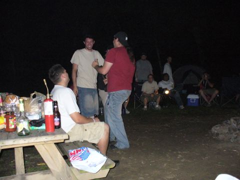 1991 Ford Probe - People are enjoying a night out at a campsite with a picnic table laden with drinks and snacks.