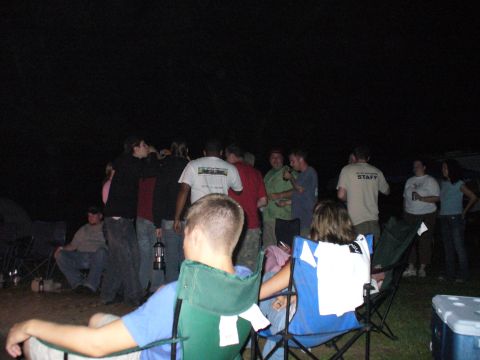 1991 Ford Probe - A group of people are seen socializing at a campsite during the night, with some sitting in chairs and others standing.