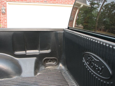 1991 Ford Bronco - Close-up of the Ford logo on the side of a truck bed, with a reflection visible in the window.