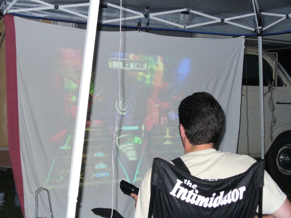 Man playing video game with projected graphics, white van visible behind screen