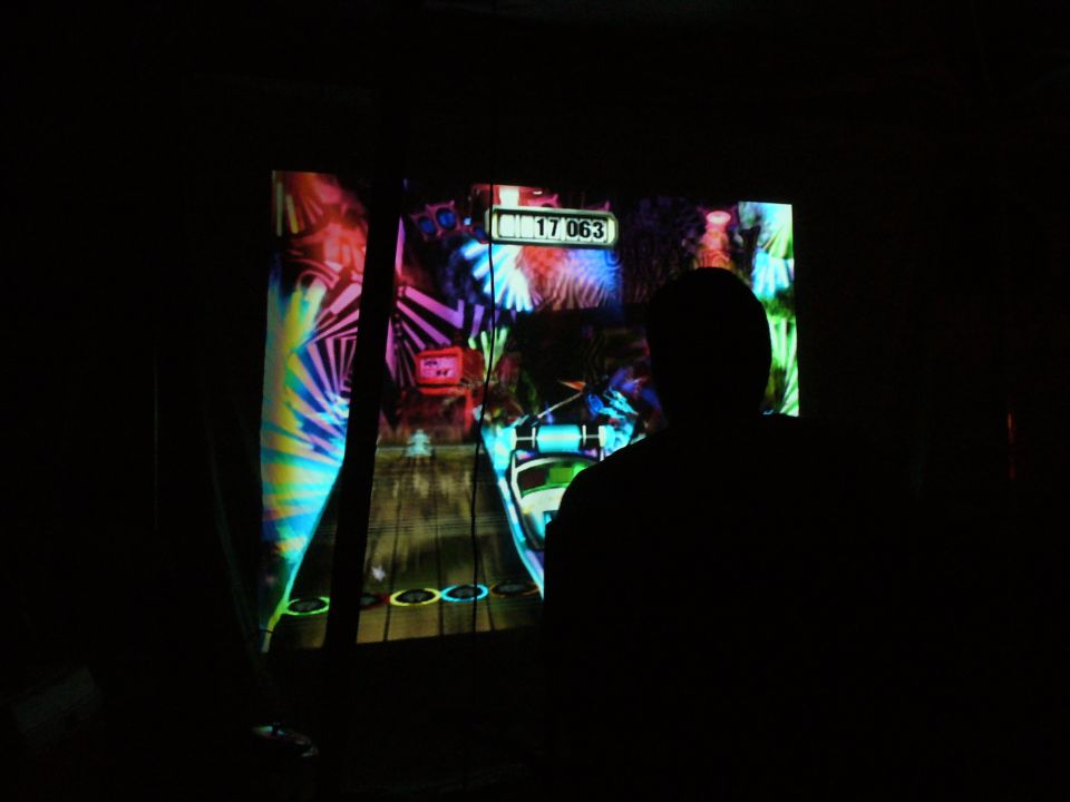 Person silhouetted against a brightly lit video game screen displaying colorful graphics and a score of 17063