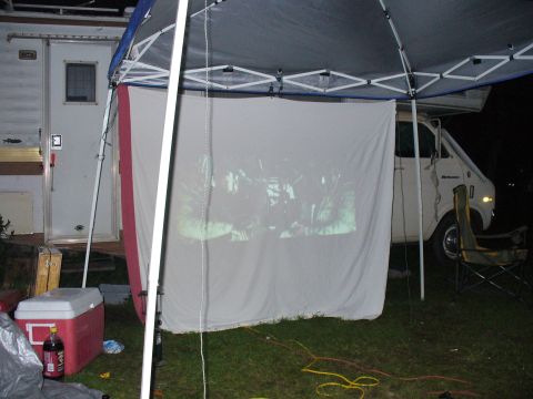 1991 Ford Probe - A white van is parked outdoors under a canopy, with a projection screen set up in front of it.