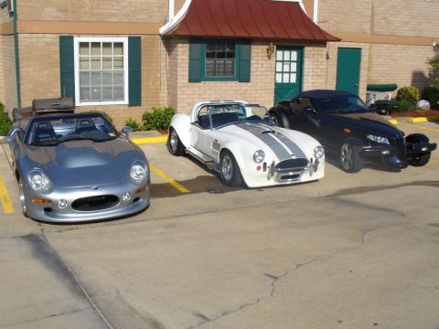 1995 Ford Thunderbird - Three distinct sports cars are parked side-by-side in a lot outside a brick building.