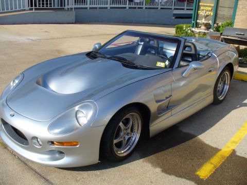 1995 Ford Thunderbird - A silver convertible sports car is parked outdoors, with a sign for discounted show tickets in the background.