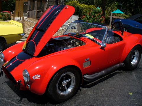 1995 Ford Thunderbird - A red convertible sports car with black racing stripes is displayed at a car show, with its hood open to reveal the engine.