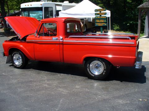 1995 Ford Thunderbird - A classic red pickup truck is displayed outdoors with its hood up, near an RV and a vendor tent.