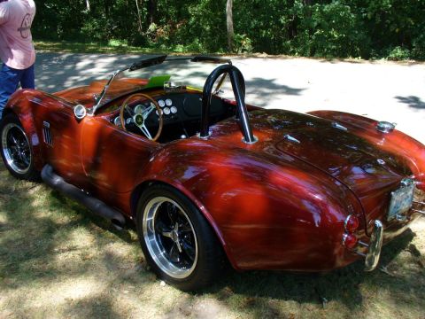 1995 Ford Thunderbird - A red convertible sports car with a black roll bar and side exhaust pipes is parked outdoors on grass.