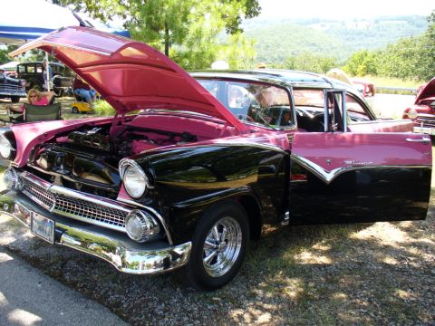 1995 Ford Thunderbird - A classic two-tone pink and black Ford Fairlane is displayed with its hood and driver's door open at an outdoor car show.