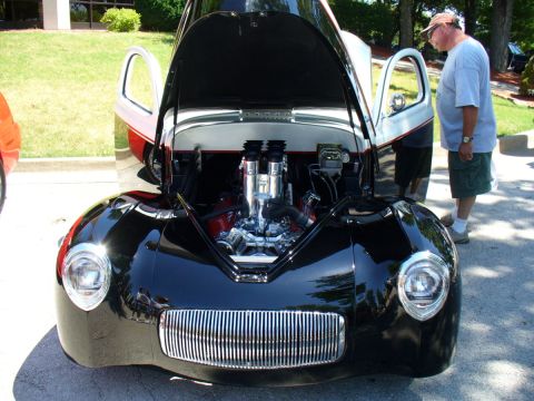 1995 Ford Thunderbird - A man looks at the engine of a custom hot rod displayed at a car show.