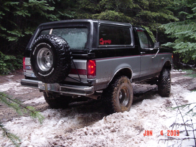 Rear quarter of black-over-gray Ford Bronco with rear-mounted spare on snowy ground