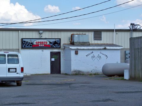 1971 Ford Ranchero - A white van is parked outside a building that has a 'Sports Bar' sign and NASCAR-themed decorations.