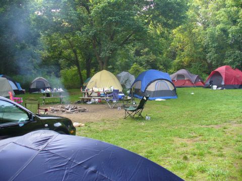 1991 Ford Probe - A black car is parked at a campsite, surrounded by tents and a campfire, with trees in the background.