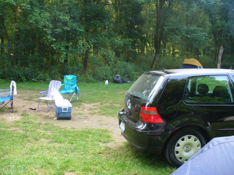 1991 Ford Probe - Campsite scene with a black hatchback, chairs, and tents set up in a wooded area.