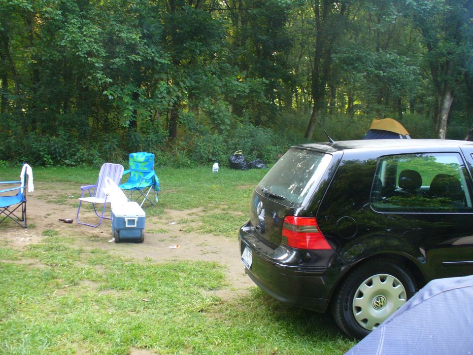 Black hatchback parked at a campsite with chairs and tents in the background