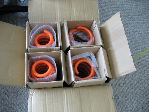 2006 Mazda 6 - A set of four orange coil springs are shown, each individually wrapped and boxed within a larger cardboard container.