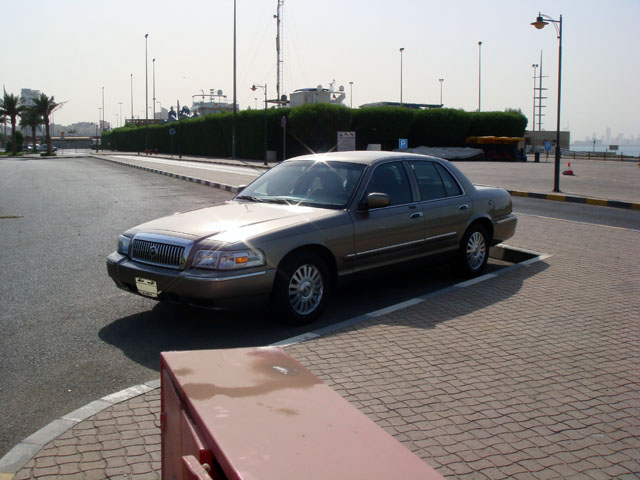 Gold four-door sedan parked in empty lot near waterfront, 3/4 front view