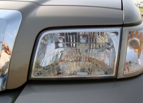 2007 Mercury Grand Marquis - Close-up of a tan vehicle's headlight and grille, showing details of the front end.