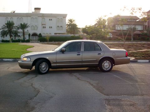 2007 Mercury Grand Marquis - A gold Mercury Grand Marquis is parked on asphalt with a building and trees in the background.
