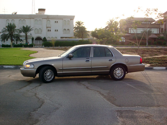 Gold Mercury Grand Marquis parked outside a large building