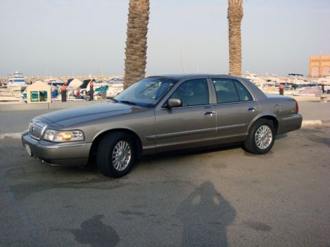 2007 Mercury Grand Marquis - A gray 2007 Mercury Grand Marquis sedan is parked near a marina with boats in the background.