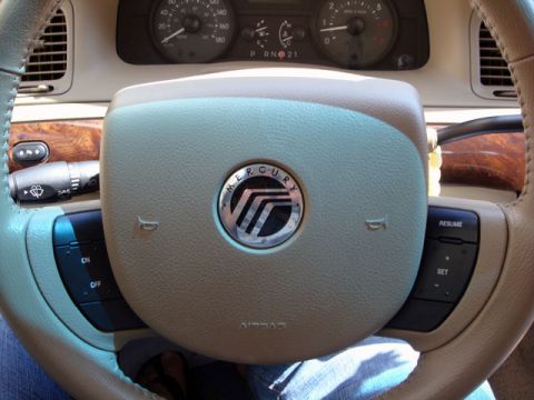 2007 Mercury Grand Marquis - Close-up of a tan leather-wrapped steering wheel with the chrome Mercury emblem on the airbag center, wood-grain trim, cruise and audio but…