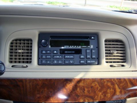 2007 Mercury Grand Marquis - Close-up of a beige/tan center dashboard console showing the factory AM/FM radio and cassette/CD player with a green digital clock reading…