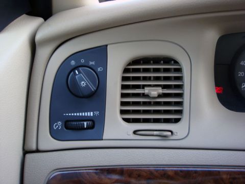 2007 Mercury Grand Marquis - A close-up of a car's dashboard showing the round rotary headlight switch with lighting icons and a dash-brightness slider, beside a tan ai…