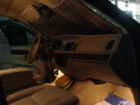 2007 Mercury Grand Marquis - Dimly lit interior of a Mercury Grand Marquis shown from the passenger side, showing the beige dashboard with woodgrain trim, steering whee…