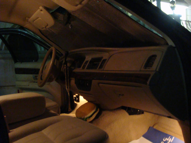 Dark interior of a Grand Marquis with beige dash, woodgrain trim, and a burger on the floor