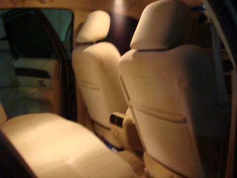 2007 Mercury Grand Marquis - Dim interior shot taken from the rear seat of a sedan, looking forward at the backs of two tan leather front bucket seats with headrests an…