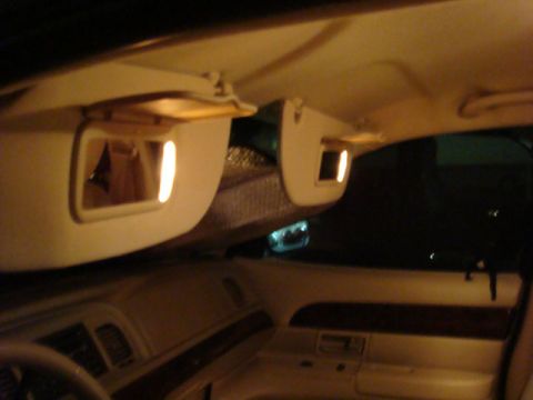 2007 Mercury Grand Marquis - Night interior shot of a light tan cabin with both sun visors flipped down and their illuminated vanity mirror lights switched on, showing…