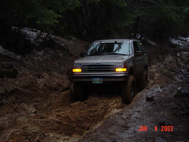 Tan Ford Explorer with headlights on working through a deep muddy washout in the woods
