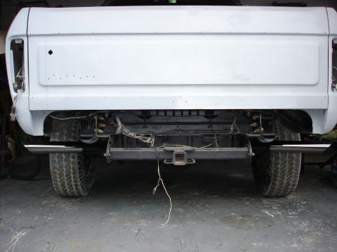 1979 Ford Bronco - This white pickup truck is shown from the rear, dual exhaust pipes and a trailer hitch, with its body appearing to be prepped for paint.
