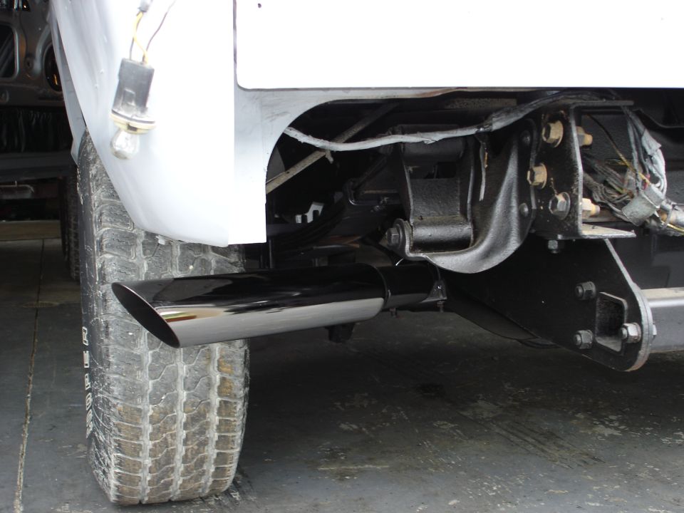 Rear tire and chrome exhaust pipe on a white vehicle's undercarriage