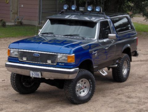 1987 Ford Bronco - This lifted 1987 Ford Bronco features a two-tone paint scheme with flame decals and auxiliary lights on the roof.