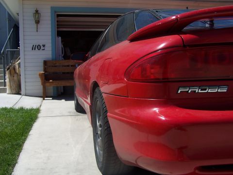 1994 Ford Probe - A red coupe with a spoiler is parked in front of a garage, showing the rear badging.