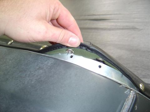 1986 Ford Bronco - Close-up of a hand pulling back black upholstery to reveal a metal edge with mounting holes and a rivet, over a green backing material. App…