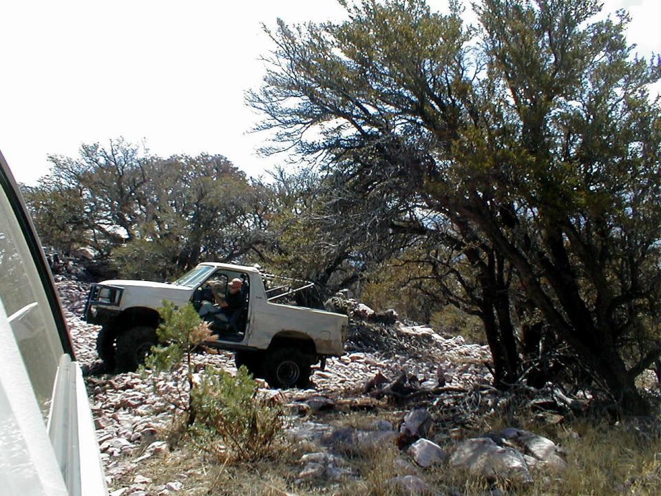 White pickup truck with lifted suspension and off-road tires driving on a rocky terrain