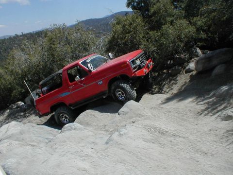 1996 Ford Bronco - A red off-road SUV navigates a challenging rocky trail on a sunny day.