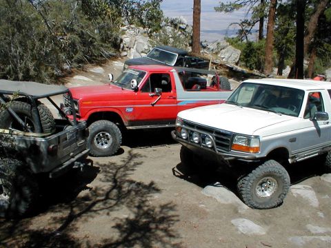 1996 Ford Bronco - Three off-road SUVs are parked on a dirt trail in a mountainous area.