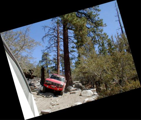1996 Ford Bronco - A red off-road SUV navigates a challenging rocky terrain under a clear blue sky.