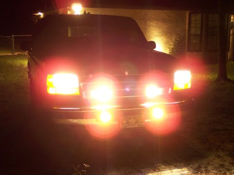 1996 Ford Bronco - A dark Ford Bronco is parked at night, its headlights and fog lights illuminated.