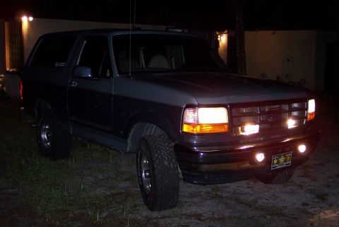 1996 Ford Bronco - This Ford Bronco is parked in front of a building at night, with its headlights on.