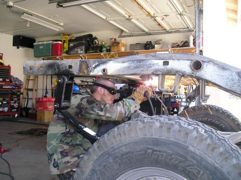 1986 Toyota Hilux - A person is welding a vehicle frame in a garage, with large tires in the foreground.