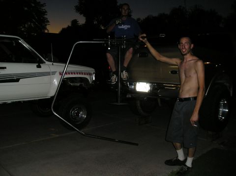 1986 Toyota Hilux - Two pickup trucks are parked outside at dusk, with two men interacting with them.