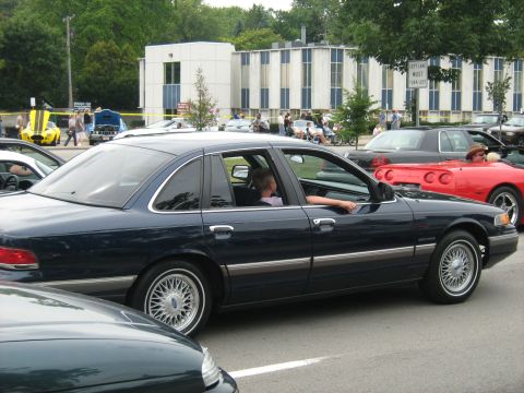 1988 Mercury Grand Marquis - A dark blue sedan is seen from the side at an outdoor event with other vehicles and buildings in the background.
