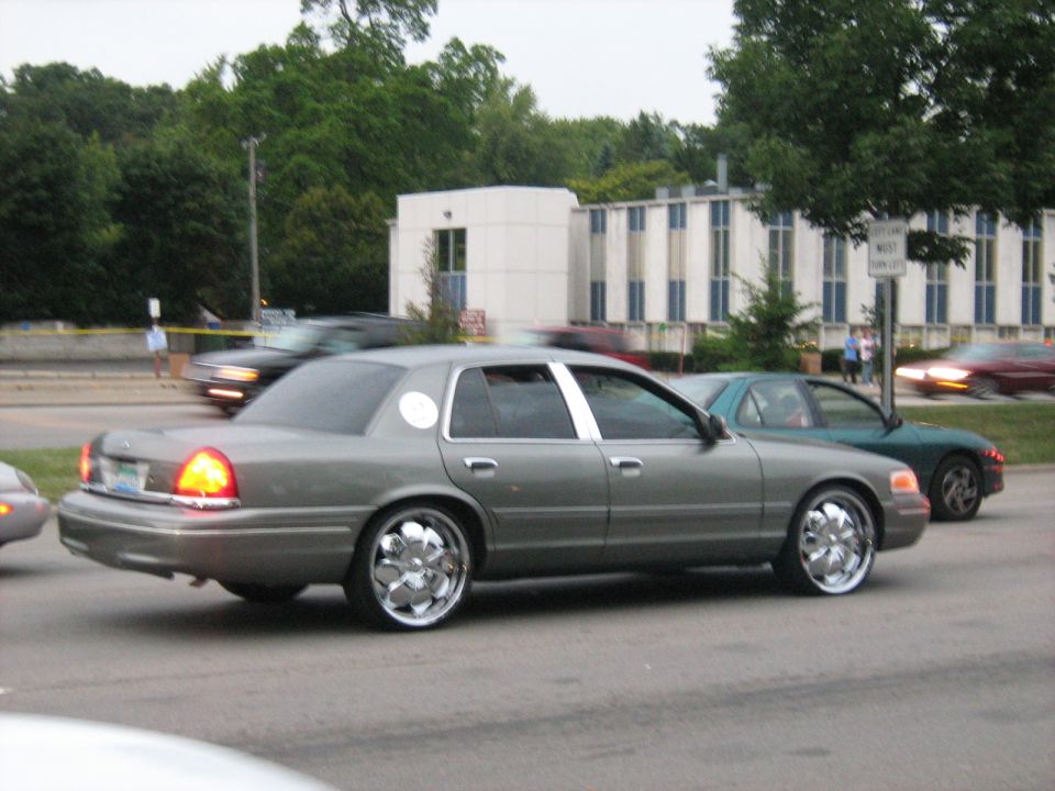 Gray Ford Crown Victoria sedan on large chrome rims at a roadside