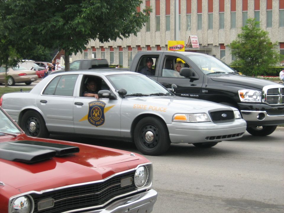 Silver Michigan State Police sedan, front quarter view, with a black pickup truck behind it