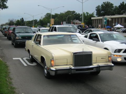 1988 Mercury Grand Marquis - A line of vehicles, including a cream-colored Lincoln Continental Mark VII, drives down a street.