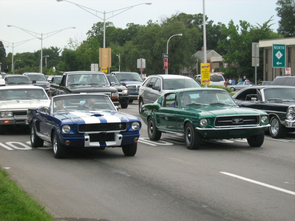 Green 1967 Ford Mustang fastback driving in traffic, front view